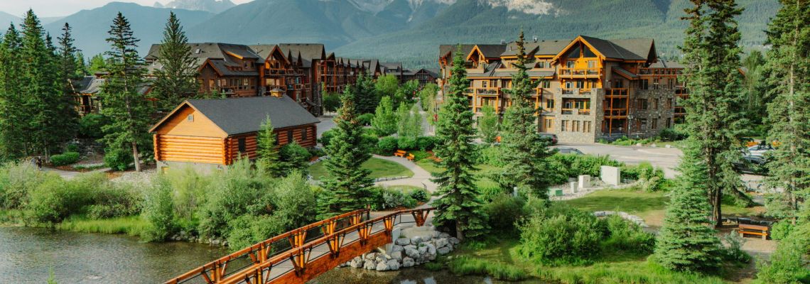 Aerial view of Spring Creek village in Canmore, with mountain lodges, evergreens, and a paved walking or biking paths.