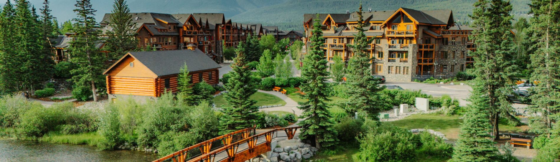Aerial view of Spring Creek village in Canmore, with mountain lodges, evergreens, and a paved walking or biking paths.